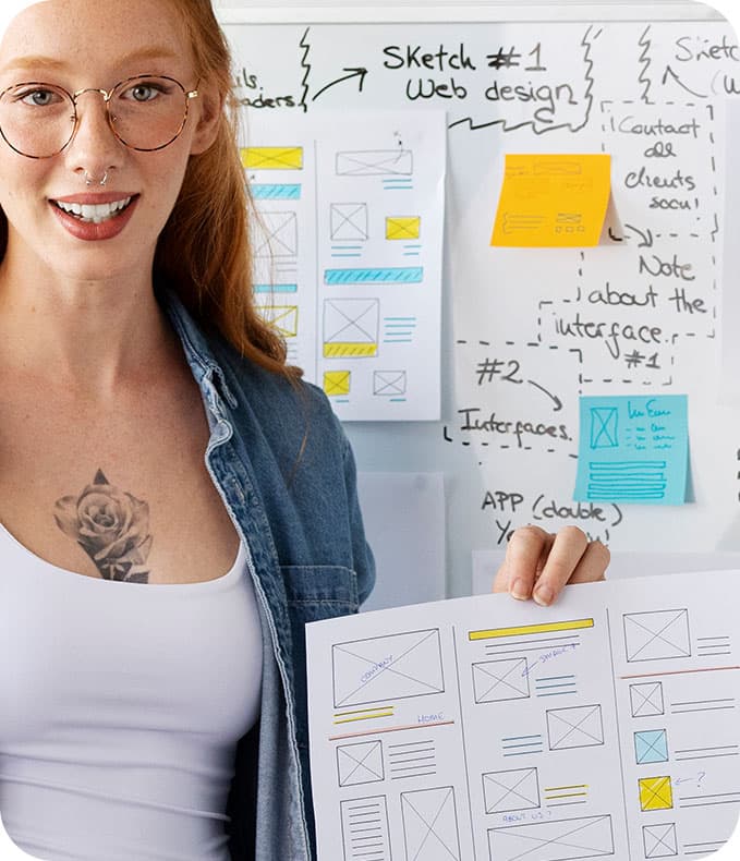 Person holding UI wireframes and sticky notes on a whiteboard